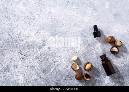 Natürliches Macadamia-Nussöl in einer Flasche. Kosmetiköl. Draufsicht Macadamianüsse auf grauem Hintergrund Stockfoto