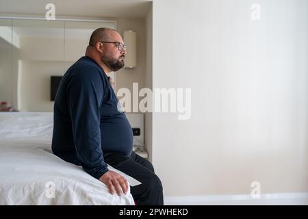 Ruhiger, schläfriger Mann, der morgens zu Hause aufwacht und im Bett sitzt, bereit für den neuen Tag. Stockfoto