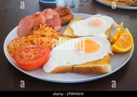 Australisches Frühstück mit Spiegeleiern auf Toast, Speck, Würstchen, Spaghetti, Tomaten und Orangenscheiben Stockfoto