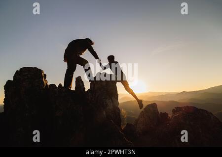 Silhouette der Teamarbeit zweier Wanderer, die sich auf dem Gipfel des Bergsteigerteams gegenseitig helfen. Teamwork Freundschaft Wandern hilft einander Vertrauen Assistentin Stockfoto