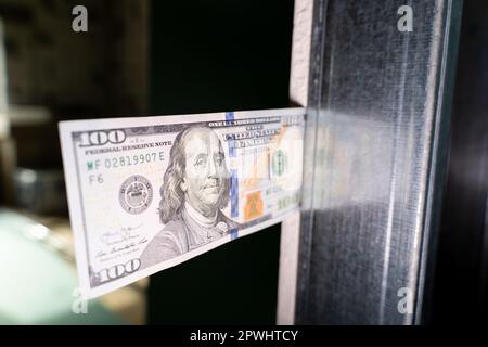 Hundert Dollar in bar, in eine unfertige Gipskarton- und Metallprofilwand gesteckt, Nahaufnahme Stockfoto