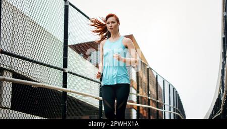 Geh direkt auf deine Ziele zu. Eine sportliche junge Frau, die beim Laufen in der Stadt Musik hört. Stockfoto