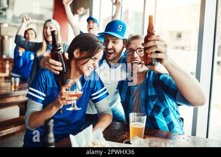 Team Blau bis zum Ende eine Gruppe von Freunden, die Bier trinken, während sie sich ein Sportspiel in einer Bar anschauen. Stockfoto