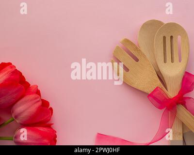 Rote Tulpen mit Küchenutensilien auf pinkfarbenem Hintergrund mit Kopierbereich. Grußkarte zum Frauen- und Muttertag. Glückwunschbrief zum Geburtstag. Utensil Stockfoto