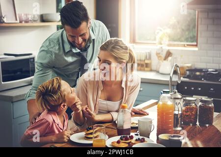 Er ist so ein braver Junge. Ein kleiner Junge, der mit seinen Eltern frühstückt. Stockfoto