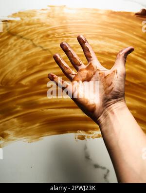 Gesalzene Karamellsauce auf der Tischplatte verschmiert. Hand und Tischplatte mit Karamell befleckt. Foto von oben mit Speisen. Schmutzige Hand Stockfoto