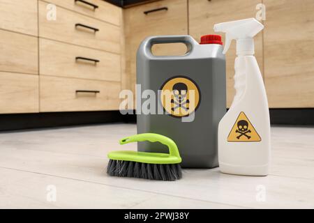 Flaschen mit giftigen Haushaltschemikalien mit Warnschildern und Bürste auf dem Boden im Innenbereich, Platz für Text Stockfoto