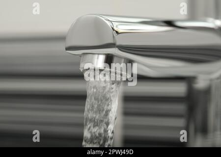 Wasser fließt aus dem Hahn auf verschwommenem Hintergrund, Nahaufnahme Stockfoto