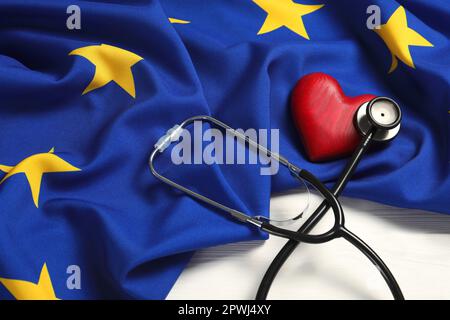 Stethoskop, rotes Herz und Flagge der Europäischen Union auf weißem Holztisch Stockfoto