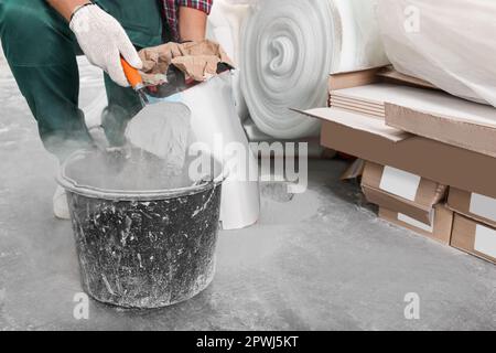 Arbeiter mit Zementpulver und Kelle mischt Beton in Eimern in Innenräumen, Nahaufnahme Stockfoto