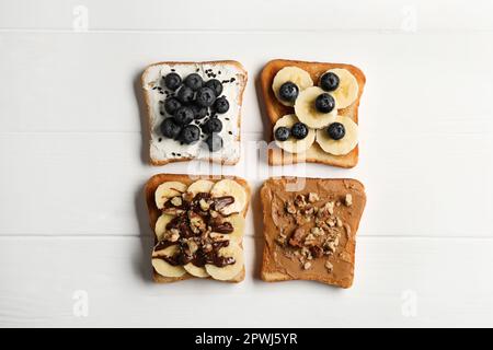 Verschiedene süße köstliche Toasts auf weißem Holztisch, flach liegend Stockfoto