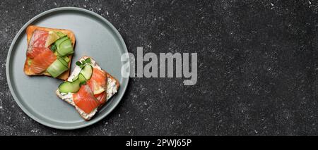 Leckere Toasts mit Lachs, Frischkäse und Gurke auf einem dunklen Tisch, Blick von oben mit Platz für Text. Bannerdesign Stockfoto