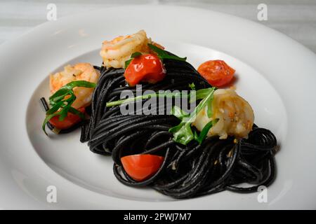 Spaghetti al Nero di Seppia con Gamberi, italienische Pasta mit Tintenfischtinte, Garnelen, Tomaten und Rucola Stockfoto