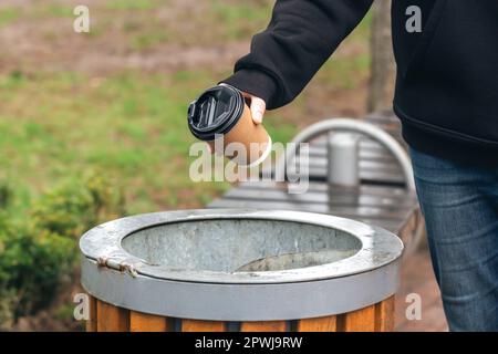 Ein Mann wirft einen Papierbecher in den Mülleimer im Park. Stockfoto