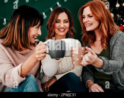 Ihr Mädchen seid mein ein und alles. Drei attraktive Frauen mittleren Alters sitzen zusammen auf einem Sofa, während sie zu Hause zu Weihnachten Kaffee trinken Stockfoto