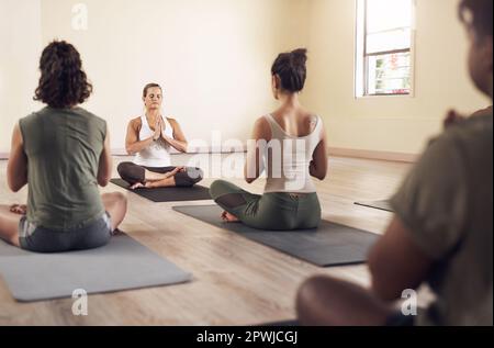 Schließ die Augen und lass das Zen übernehmen. Eine Gruppe junger Leute, die meditieren und zusammen in einem Yoga-Kurs trainieren Stockfoto