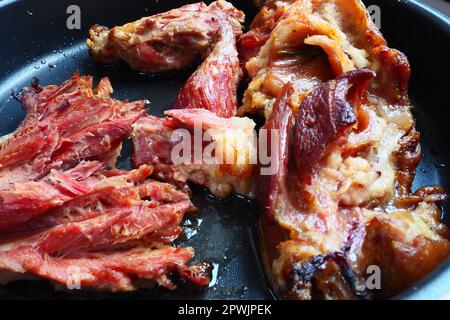 Schulter oder Knie von geröstetem, geräuchertem Schweinefleisch. Köstliches Fleisch auf einem schwarzen Backblech mit Tropfen Pflanzenöl, das aus dem Ofen genommen wurde. Schweinefleisch-Delikatesse für din Stockfoto