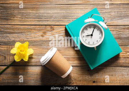 Buch, Wecker, Pappbecher und Blumen auf Holzhintergrund, Draufsicht. Stockfoto