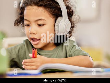 Er hat viel zu zeichnen. Ein kleiner Junge malt, während er zu Hause Musik hört Stockfoto