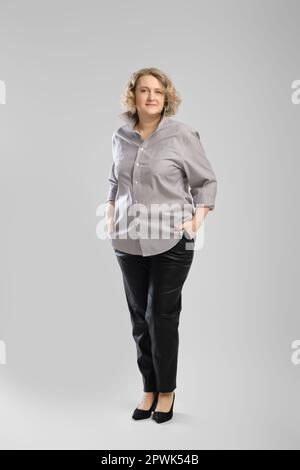 Ganzkörper-Casual-Porträt einer älteren Frau in grauem Hemd und Hose auf grauem Studiohintergrund Stockfoto