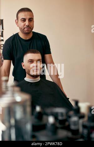 Friseur und zufriedener gutaussehender Mann vor dem Spiegel im Friseursalon Stockfoto