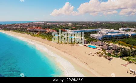 Blick aus der Vogelperspektive auf Touristen, die ein tropisches Resort im Meer genießen. Luftaufnahme des tropischen Sandstrands mit Palmen und Sonnenschirmen an sonnigen Tagen. Breit ein sauberer tropischer Strand mit weißem Sand und Sonnenschirmen. Stockfoto