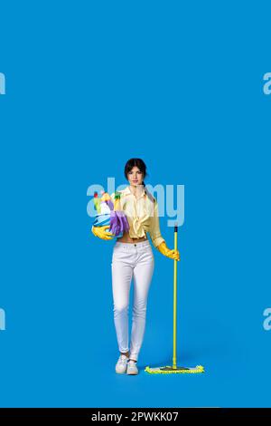 Konzertiertes seriöses Mädchen in Gummihandschuhen, Haushaltsführung und Reinigung mit Mopp und Eimer mit Reinigungsmitteln auf blauem Hintergrund. Volle Länge Stockfoto