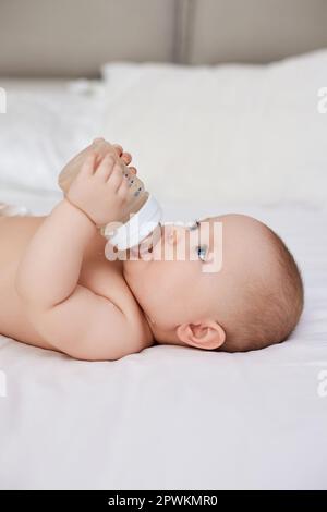 Charming Baby Mädchen liegt im Bett und trinkt Wasser aus einer Flasche Stockfoto