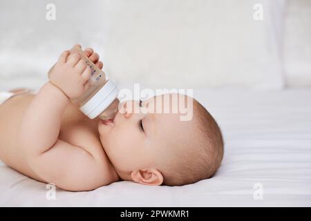 Charming Baby Mädchen liegt im Bett und trinkt Wasser aus einer Flasche Stockfoto