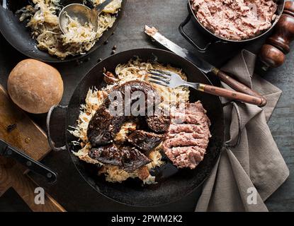 Blutiger Wurstmorcilla, gekochtes Sauerkraut und Kartoffelpüree mit Bohnen aus der Nähe. Traditionelles slowenisches Gericht mit gebratener blutiger Wurst Stockfoto