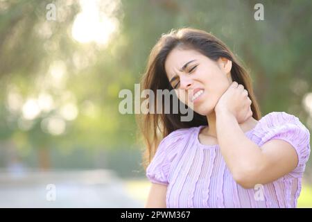 Gestresste Frau, die Nackenschmerzen hat, allein in einem Park Stockfoto