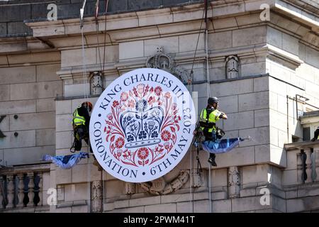 London, Großbritannien. 29. April 2023. Arbeiter neben einem König-Karl-III-Schild hängen an Seilen, nahe dem Gipfel des Admiralty Arch. Die Vorbereitungen für die Krönung von König Karl III. Sind heute in London (29. April) im Gange Es bleibt nur noch eine Woche, bis König Karl III. Am 6. Mai 2023 in Westminster Abbey gekrönt wird, neben Camilla, der Königlichen Gemahlin. Die Königsfamilie kehrt dann von Westminster Abbey zurück und fährt entlang der Mall, bevor sie auf dem Balkon des Buckingham Palace auftaucht. Kredit: Paul Marriott/Alamy Live News Stockfoto