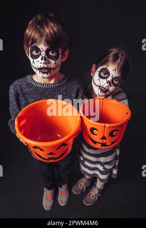 Zwei Kinder mit Totenkopf Make-up halten Kürbis Eimer an Halloween. Stockfoto