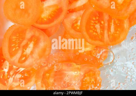 Nahaufnahme frischer Tomatenscheiben auf weißem Hintergrund. Tomatenscheiben in sprudelndem Wasser auf weißem Hintergrund, Nahaufnahme. Horizontales Bild. Stockfoto