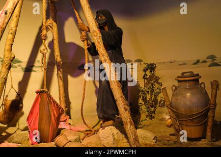 Eine Stammesfrau in einer schwarzen Burka, die Wasser aus einem Wüstenbrunnen mit einem roten Blasenbeutel holt. Ein Diorama, das eine Szene aus der Vergangenheit der Vereinigten Arabischen Emirate darstellt, im Abu DHA Stockfoto