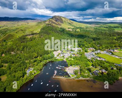 Luftaufnahme eines konischen Hügels mit Blick auf ein kleines Dorf (Balmaha, Loch Lomond, Schottland) Stockfoto