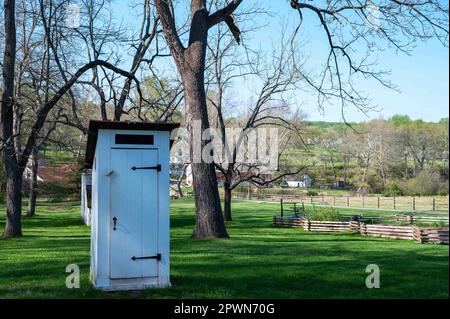 Weißes, koloniales Pennsylvania Outhouse im Gras mit Dorfhintergrund Stockfoto