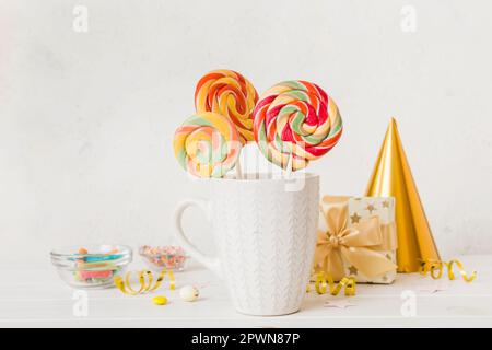 Bunte Süßigkeiten im Becher auf dem Tisch auf hellem Hintergrund. Große, geschwungene Lutscher. Kreatives Konzept eines Glases voller köstlicher Süßigkeiten aus dem Stockfoto