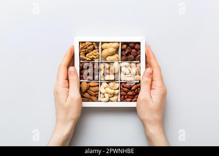 Junge Frau, die eine Kiste mit anderen Nüssen hält, Nahaufnahme. Nahaufnahme, Kopierbereich, Draufsicht, flach liegend. Walnuss, Pistazien, Mandeln, Haselnüsse und Cashews. Stockfoto