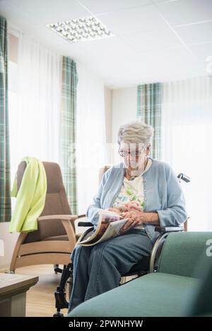 Seniorin liest Zeitschrift im Altersheim Stockfoto