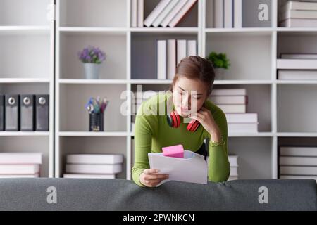 Frau sitzt zu Hause auf dem Sofa, studiert und analysiert Hausrechnungen und reicht Steuerformulare ein. Stockfoto