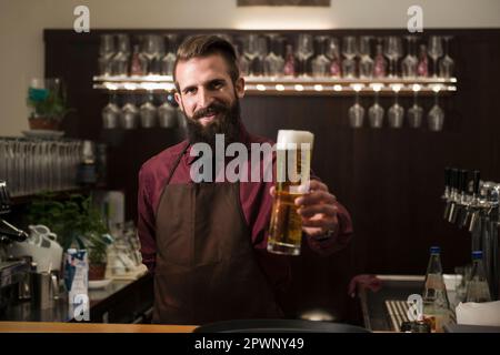 Porträt eines jungen Mannes, der ein Glas Bier anbietet Stockfoto