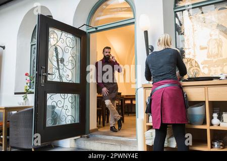 Der Restaurantbesitzer sprach mit dem Handy, während die Kellnerin an der Holztheke arbeitete Stockfoto