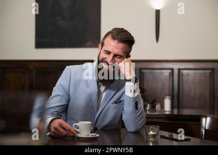 Gut gekleideter Mann, der sich eine Kaffeetasse ansieht und denkt, während er im Restaurant sitzt Stockfoto