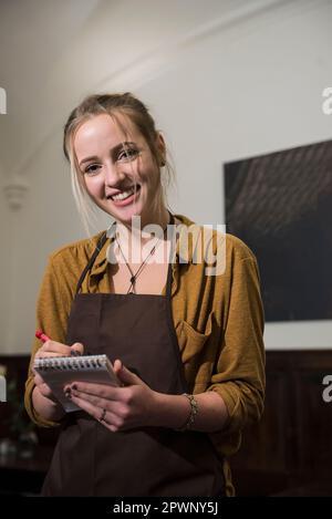 Eine lächelnde Kellnerin in der Schürze bestellt im Restaurant Stockfoto