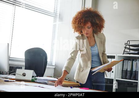 Alles wird im richtigen Ordner abgelegt. Eine wunderschöne junge Geschäftsfrau, die sich ein paar Dokumente in ihrem Büro ansieht. Stockfoto