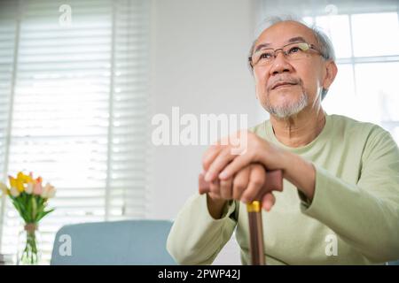 Die Hände des asiatischen alten Mannes, der zu Hause ruht, halten einen hölzernen Gehstock, ältere Hand halten den Griff des Gehstock, ältere Behinderte halten gehstock stic Stockfoto