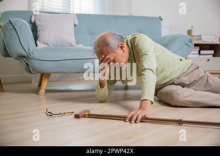Kranker älterer alter Mann, der auf dem Boden lag, weil er allein zu Hause mit einem hölzernen Spazierstock im Wohnzimmer stolperte, älterer Mann Großvater Stockfoto
