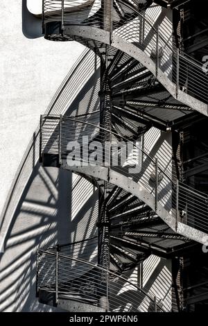 Eine Wendeltreppe oder eine Feuertreppe an der Außenwand eines Gebäudes wirft Schatten auf die Hauswand aufgrund des Sonnenlichts Stockfoto