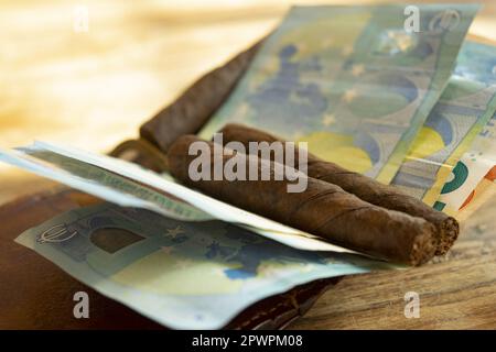 Rauchkostenkonzept mit auf Banknoten gelenkten Zigarren Stockfoto